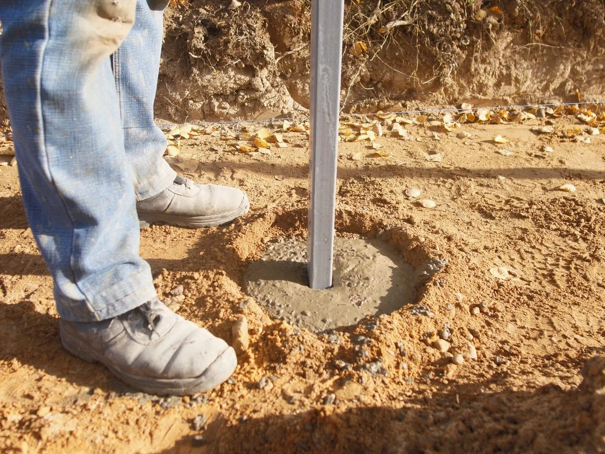 Metal fence post set in a fresh concrete footing